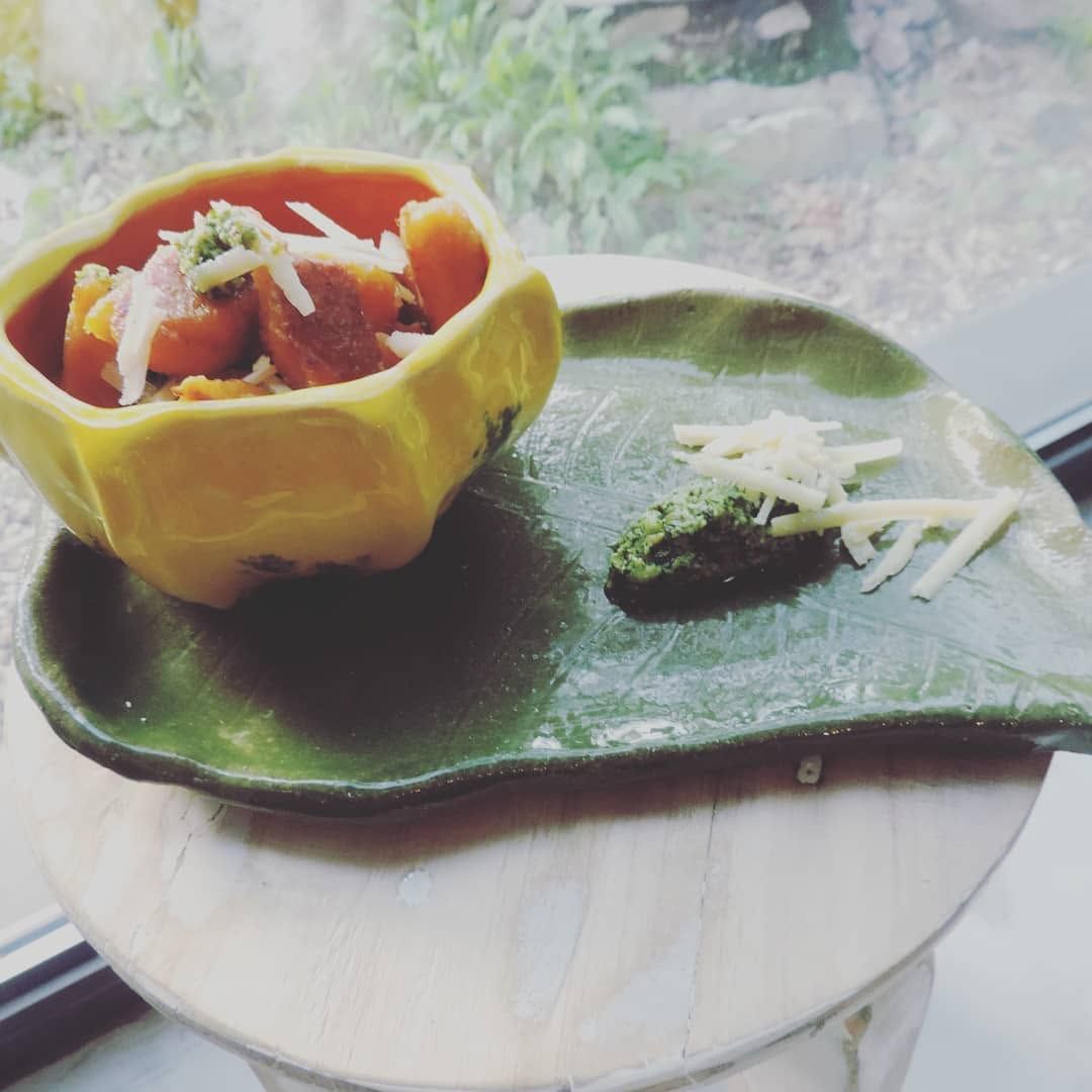 Yellow bowl with a stew on a green leaf-shaped plate, served with herbs